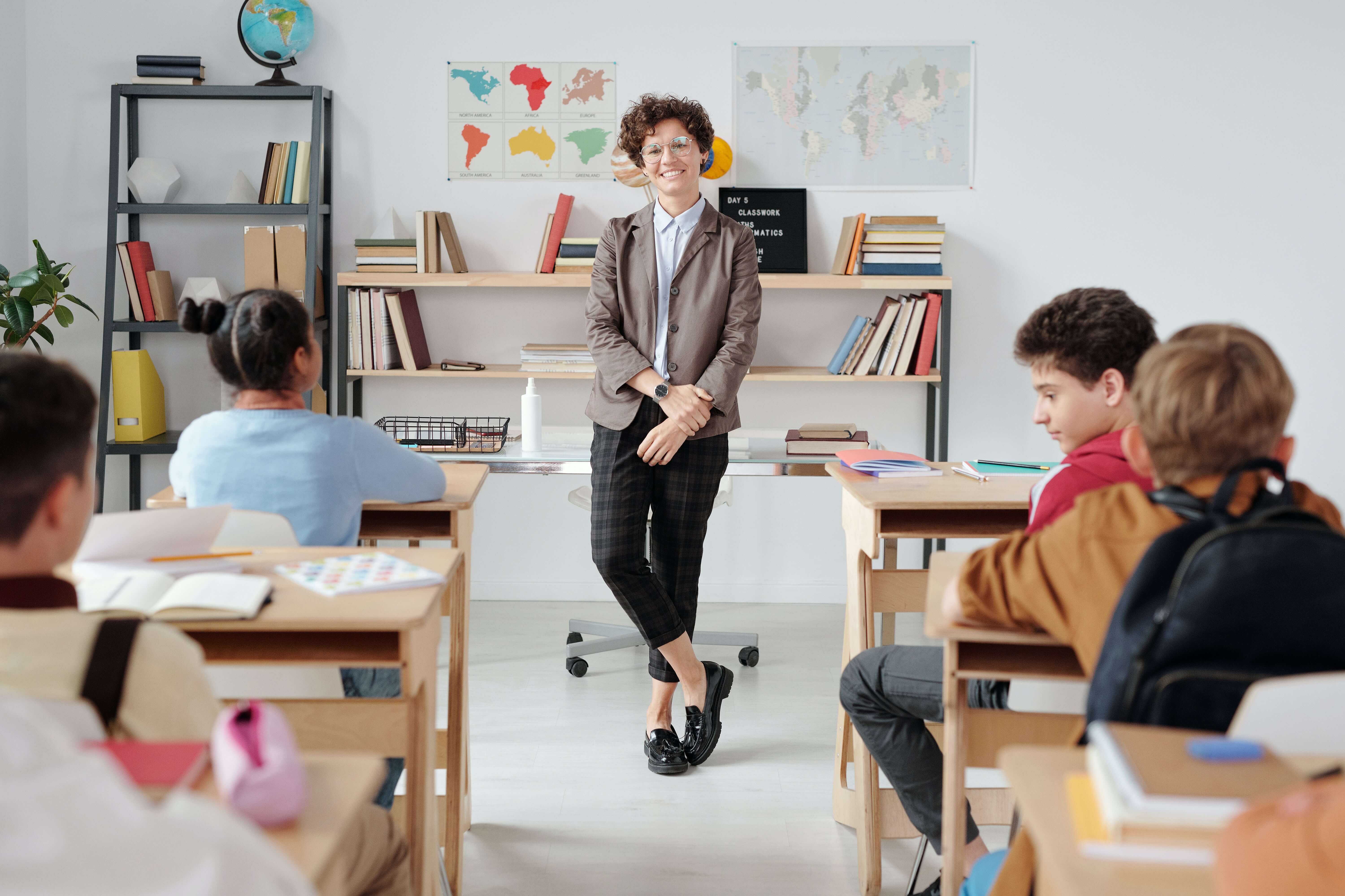 Juf met korte krulletjes staat lachend voor de klas