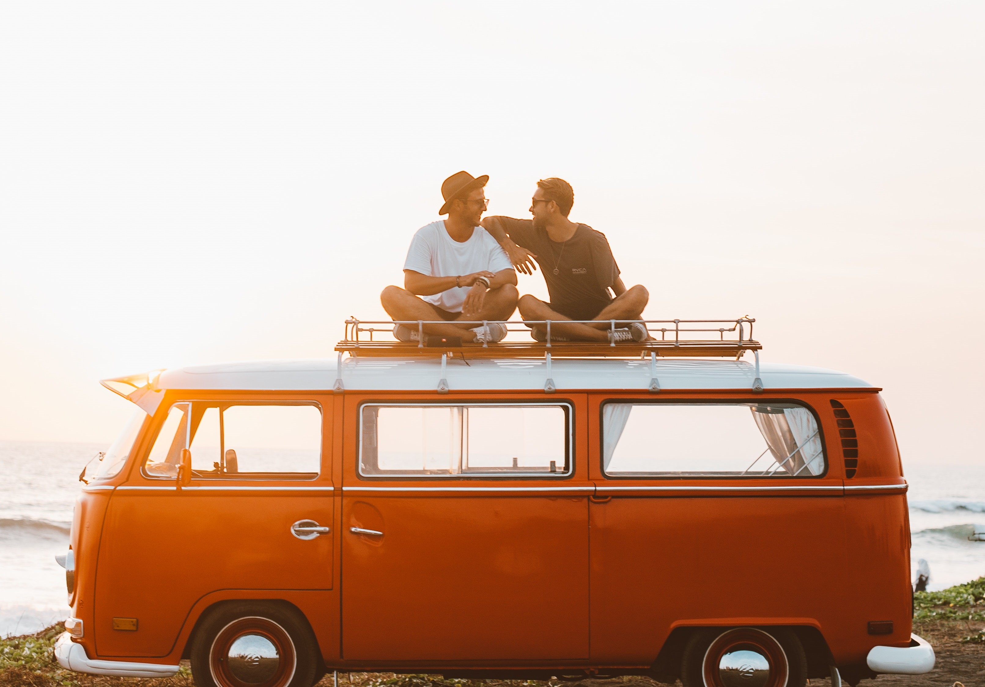 2 vrienden zitten op het dak van oranje Volkswagenbusje bij de zee