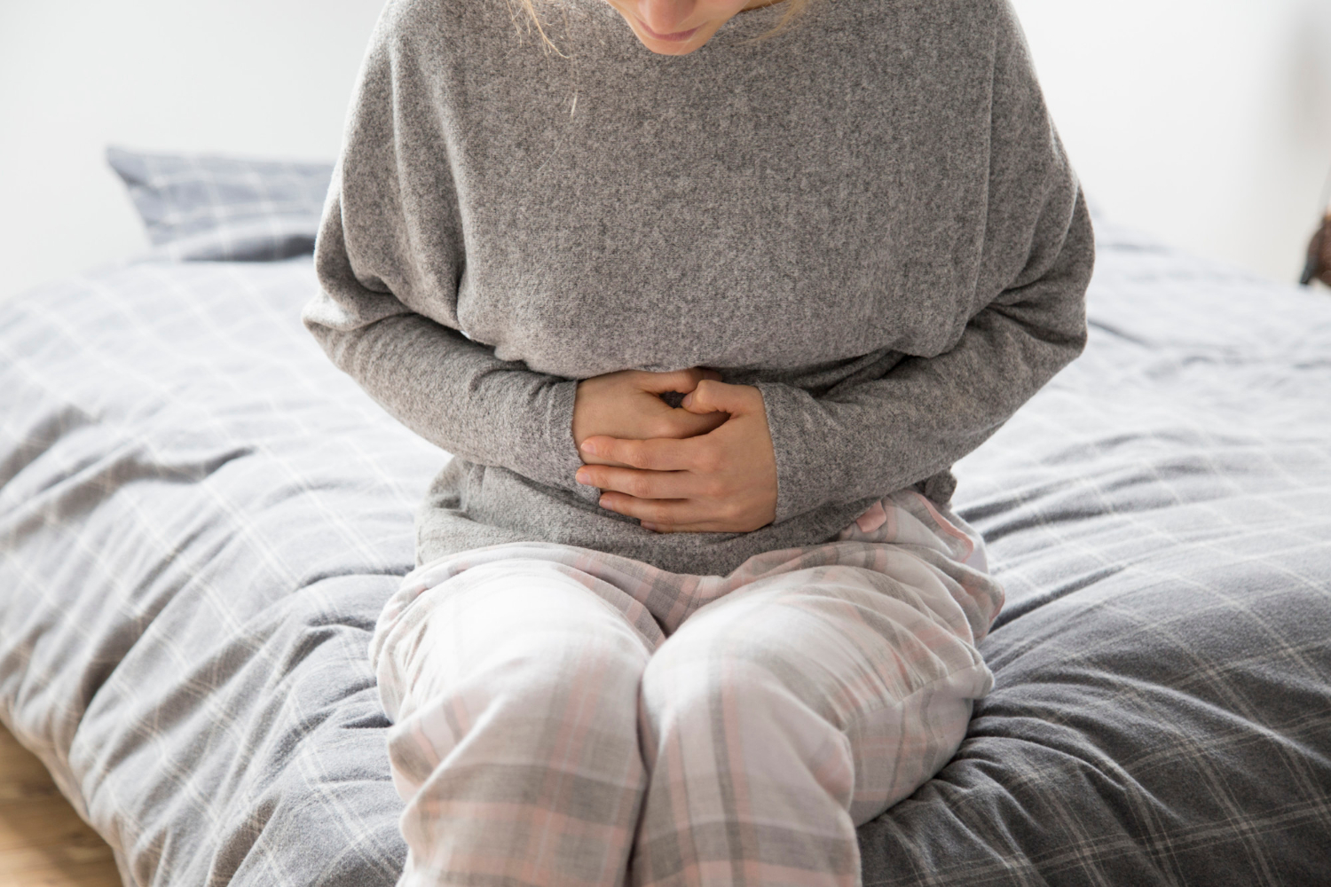 Vrouw in pyjama drukt handen op pijnlijke buik