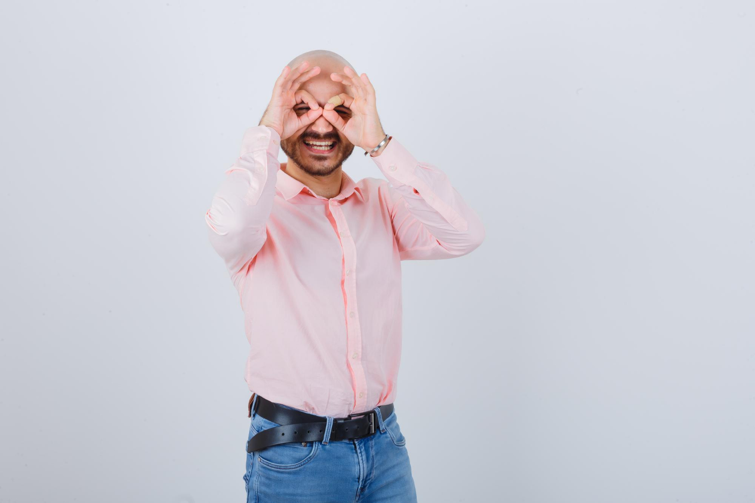 Lachende man in roze hemd maakt gek brilletje met zijn handen