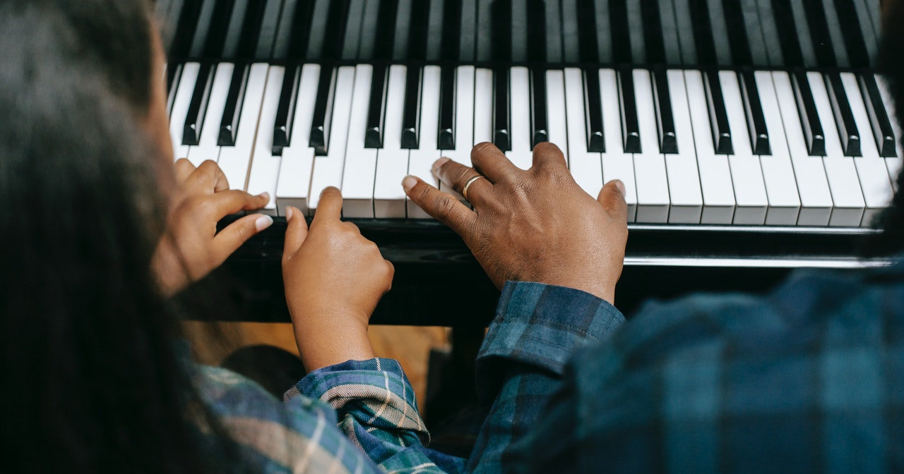 Handen van kind en volwassene samen op pianotoetsen