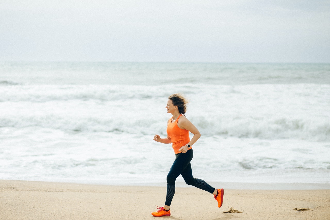 Vrouw in oranje top jogt op het strand langs het water