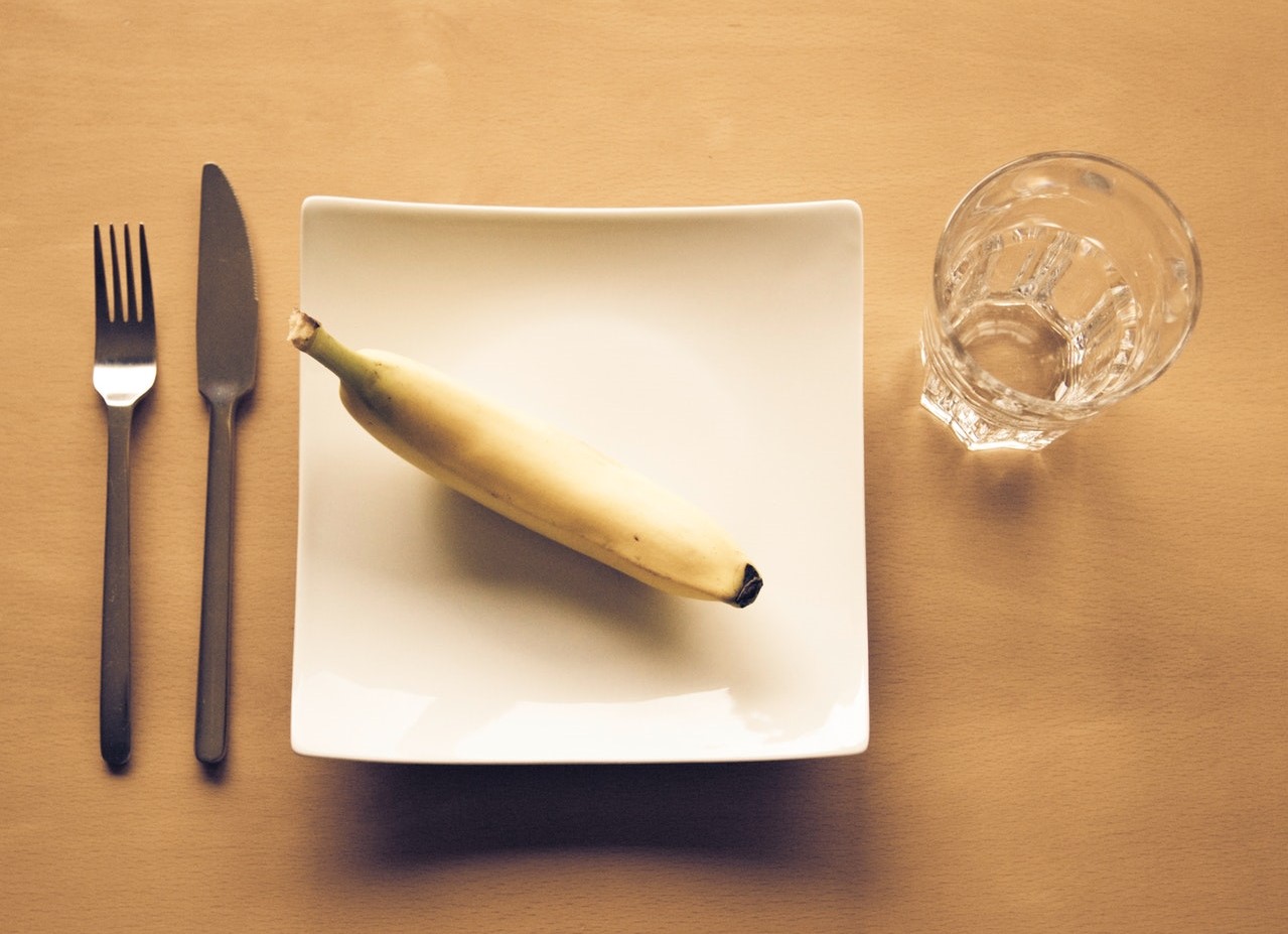 Chique vierkant bord met een banaan erop en glas en bestek ernaast