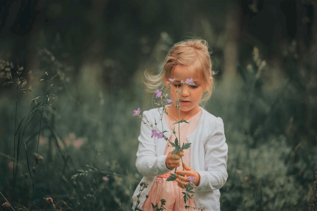 klein meisje in een veld met bloemetjes in de hand