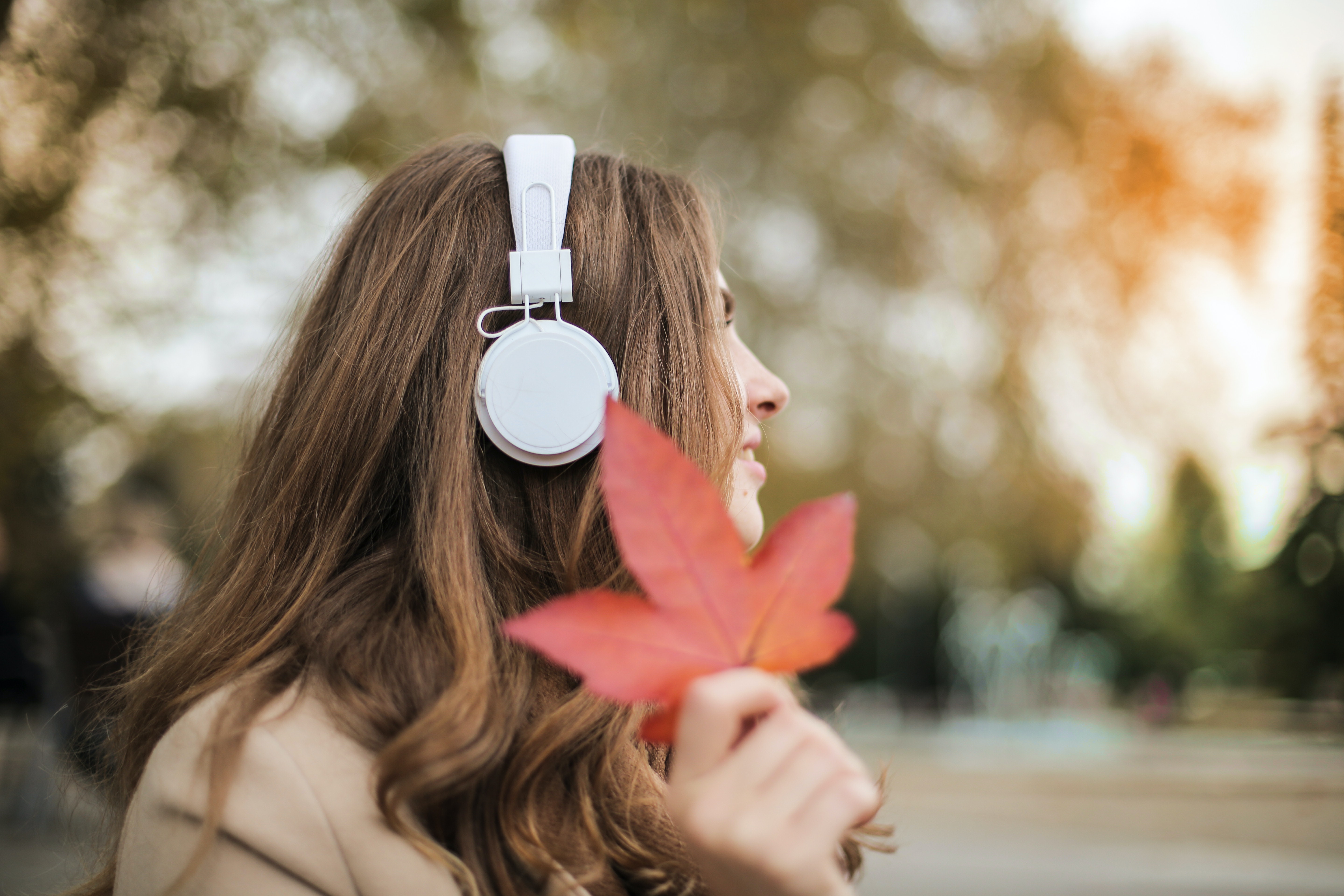 Vrouw met hoofdtelefoon en herfstblad in de hand