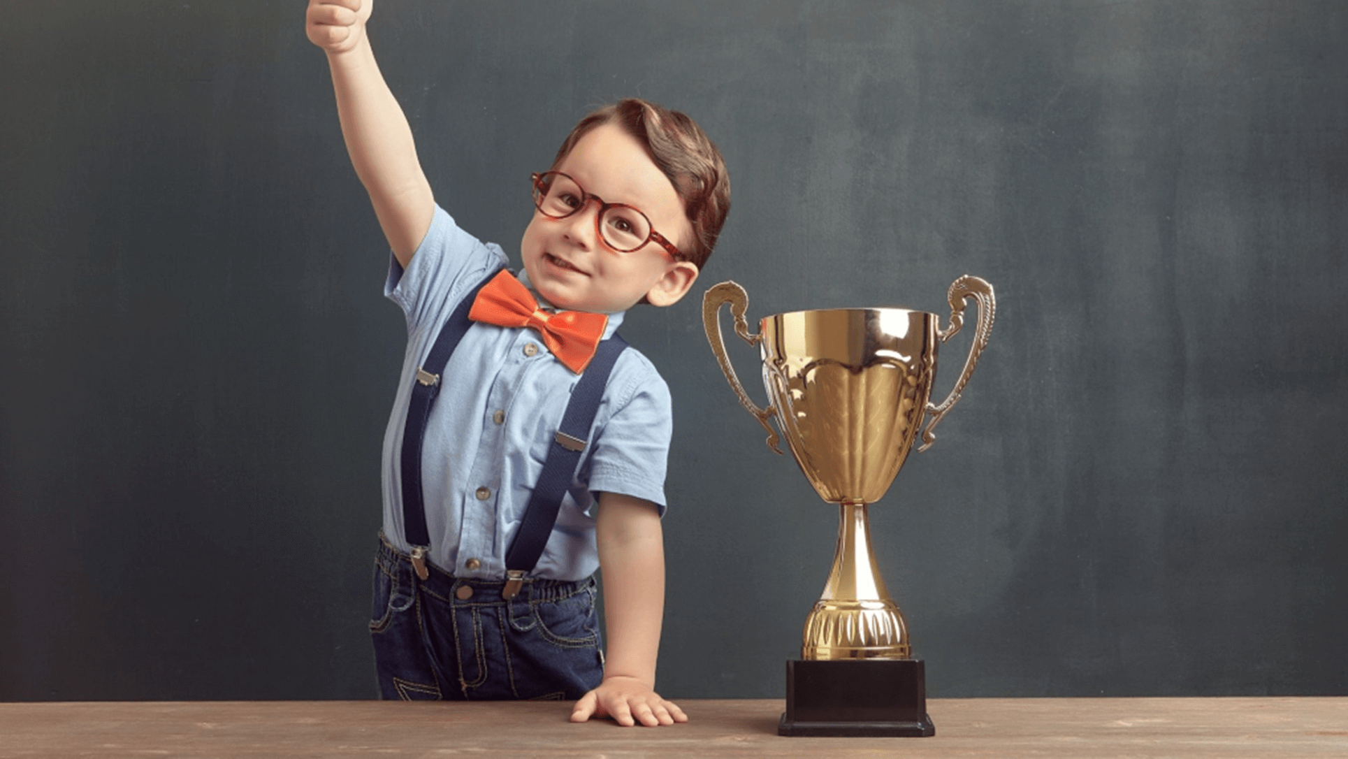 Jongetje met bril en strikje naast grote gouden beker die hij gewonnen heeft