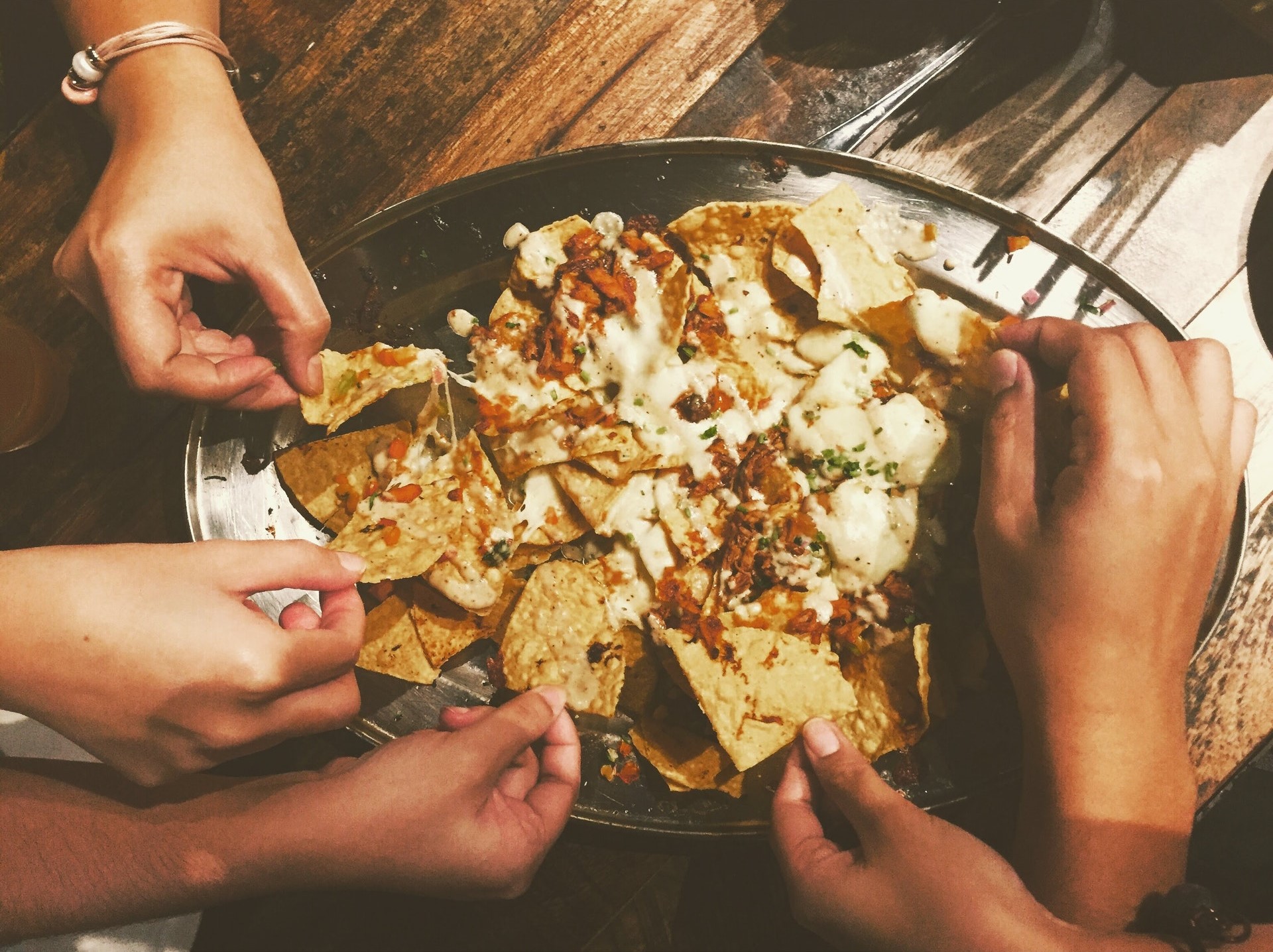 Handen grijpen naar schotel vol nachos met saus