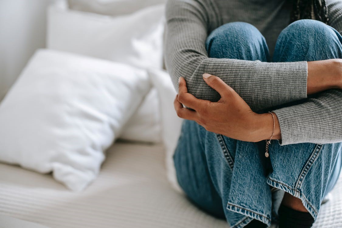 vrouw zit met handen om haar benen geslagen op bed, gezicht buiten beeld