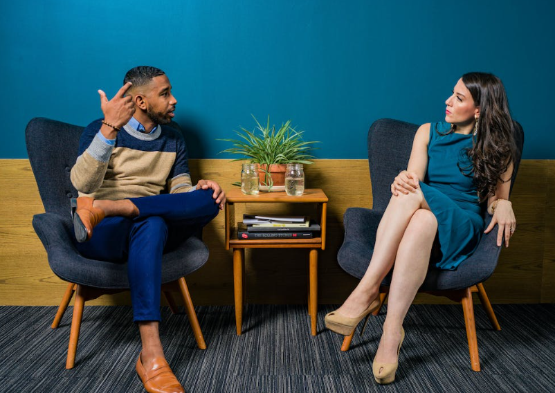 Man en vrouw in zeteltjes praten met elkaar, donker turquoise muur