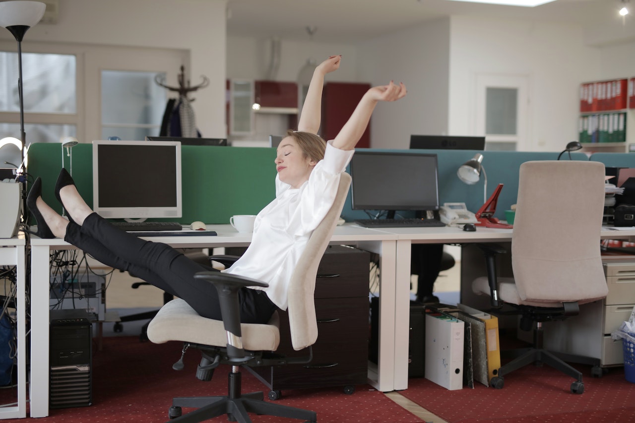 Vrouw rekt zich uit op bureaustoel op kantoor